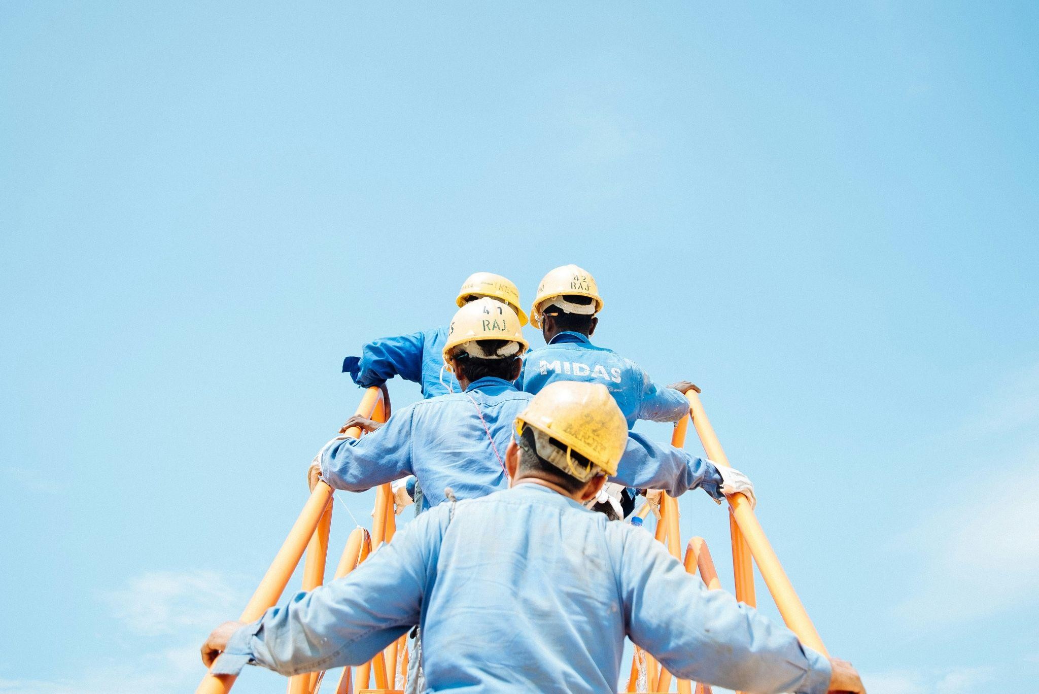 4 workers in yellow hard hats walking up a flight of yellow metal stairs.