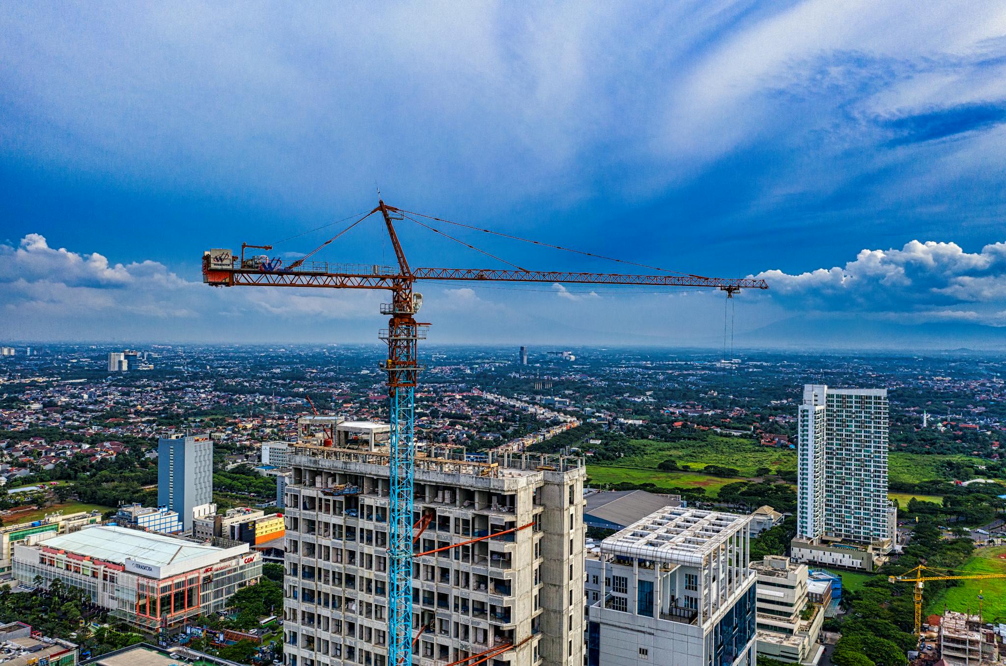 Aerial view of a construction site with a tower crane in Banten, Indonesia, under a clear blue sky.