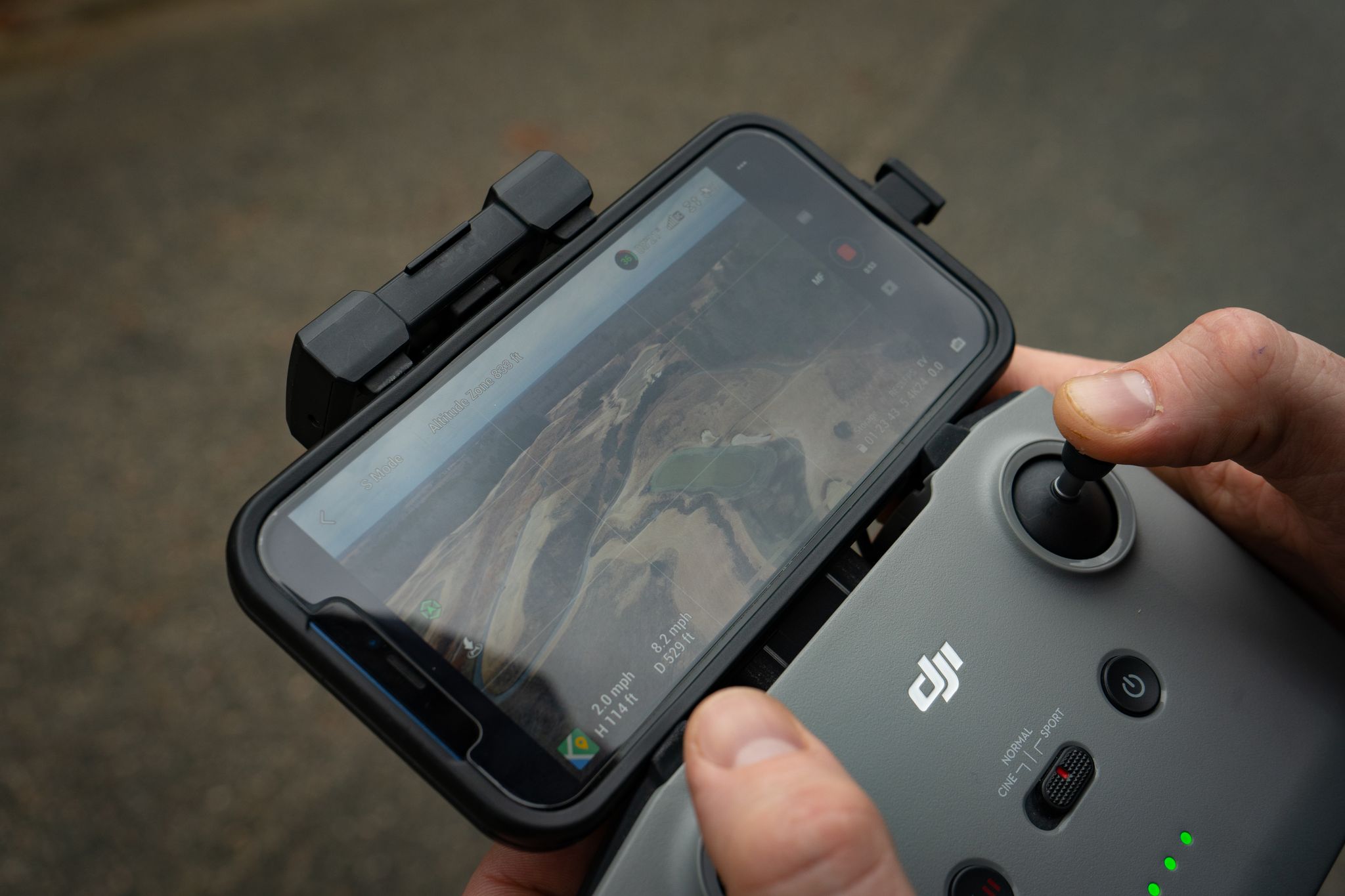 Hands controlling a drone with a smartphone display showing aerial view, demonstrating modern technology use.