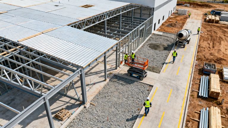 aerial photo of construction site with 3 workers below, one in a scissors lift.
